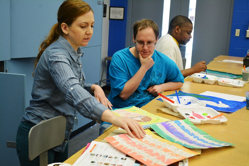 Caption: Art instructor Anastasia Cardona helps Chris Boyette select his best work for the art show.