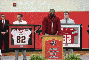 North Johnston graduate and NFL free agent, Willie Smith (front) is presented his retired jerseys from current students Reese Coley (left) and Cy Daughtry (right). Principal David West (back) looks on.