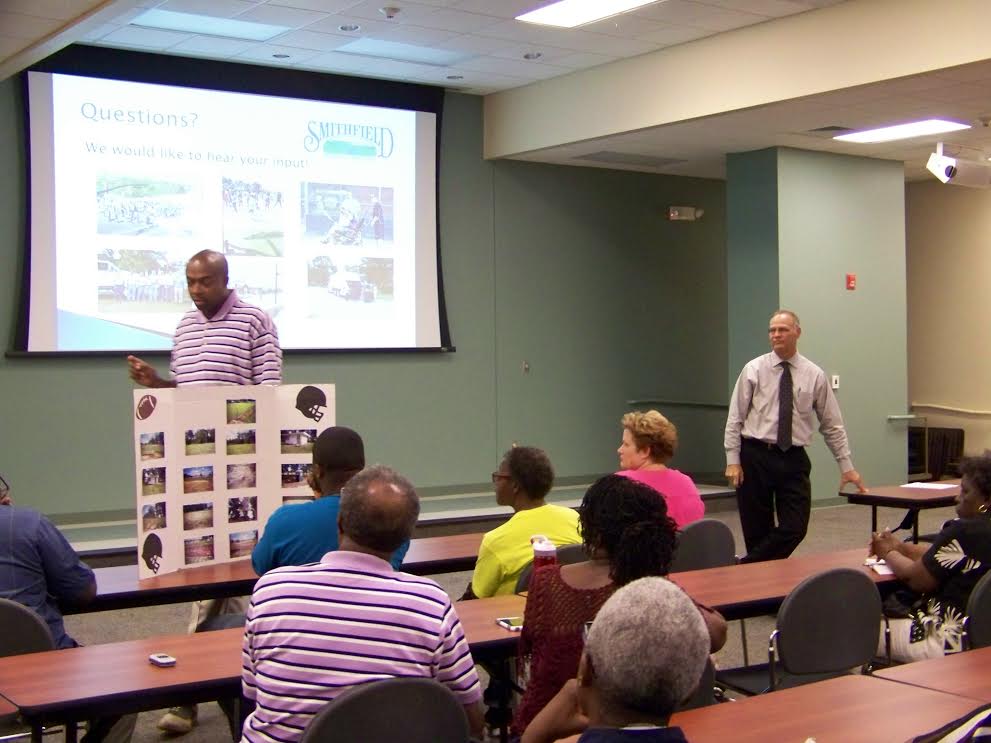 (Standing – Left to right) Town Councilman Marlon Lee shows residents photos of dilapidated recreational facilities in East Smithfield as Town Manager Michael Scott listens. JoCoReport.com Photo